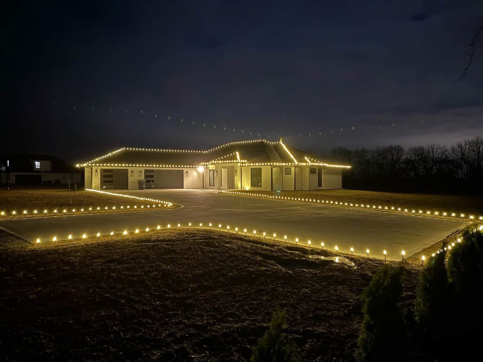 Ranch home with warm white roofline lights and a fully lit driveway and walkway at dusk