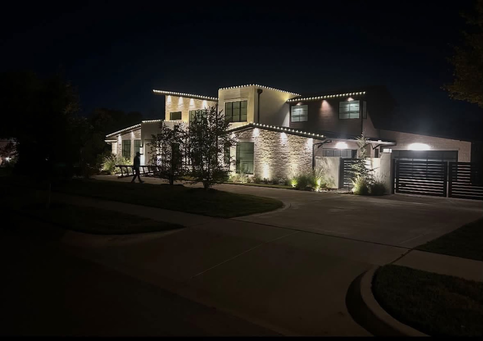 Modern two-story stone home outlined in warm white roofline lighting