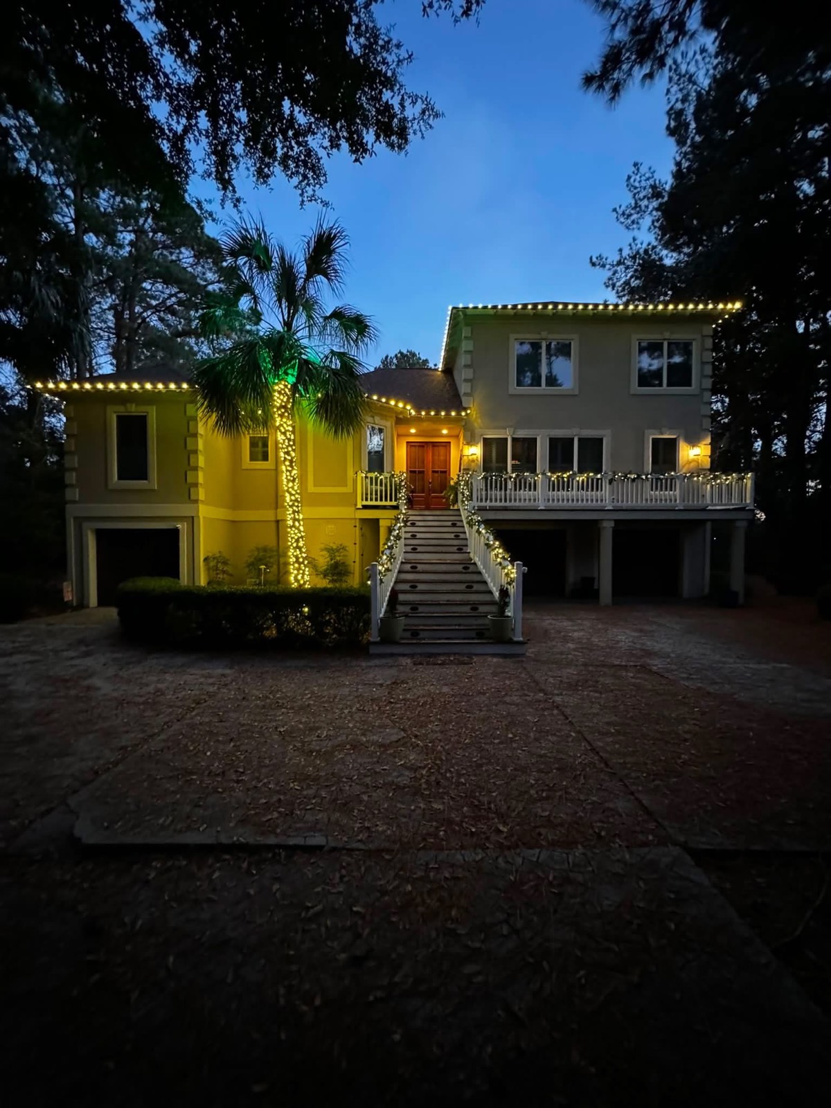 Elevated coastal home with roofline lights, a wrapped palm trunk and lit garland along the stair railings